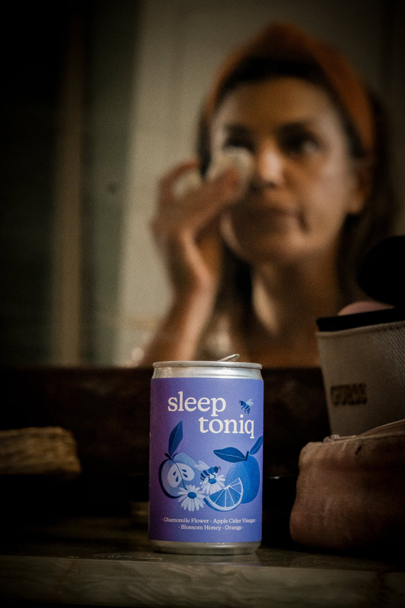 A woman sitting at a table in a dimly lit room with a can of Sleep Toniq in the foreground