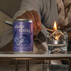Person lighting a match next to a can labeled 'sleep toniq' on a table.