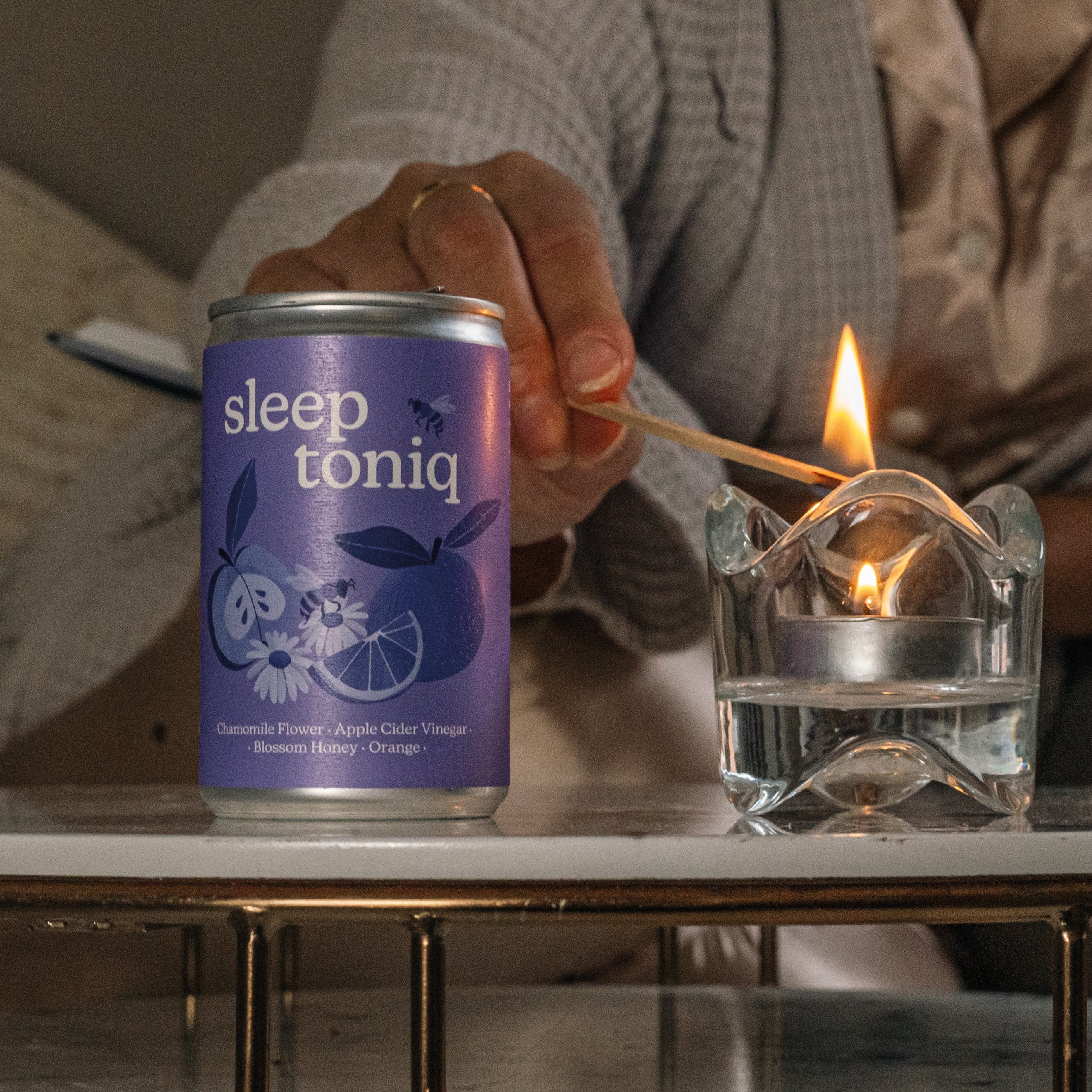 Person lighting a match next to a can labeled 'sleep toniq' on a table.
