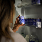 Person reaching into a refrigerator to grab a can of Sleep Toniq from a shelf.